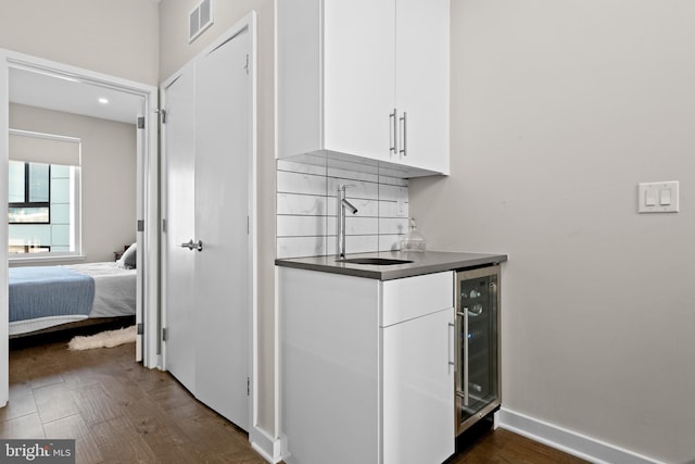 kitchen with sink, beverage cooler, backsplash, dark wood-type flooring, and white cabinetry