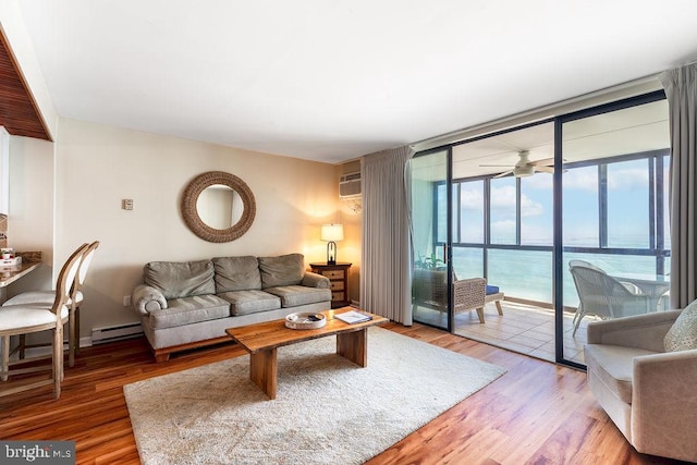 living room featuring hardwood / wood-style flooring, a water view, a baseboard heating unit, ceiling fan, and a wall of windows