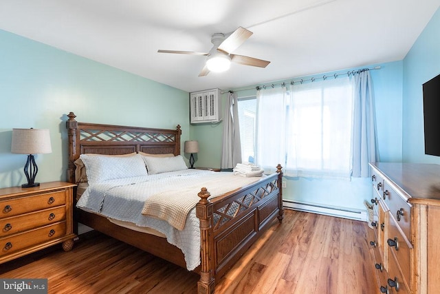 bedroom with hardwood / wood-style floors, a baseboard heating unit, and ceiling fan