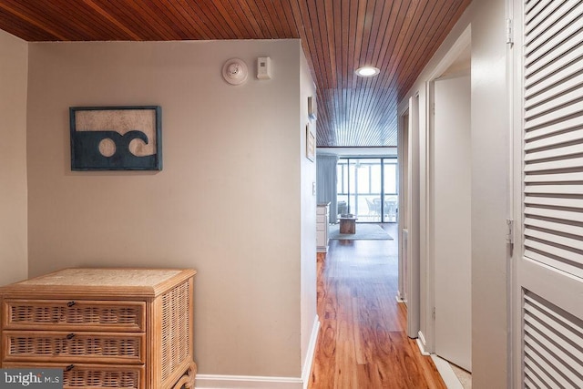 hallway featuring light wood finished floors, wood ceiling, expansive windows, and baseboards