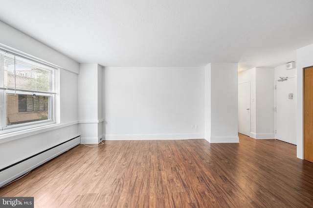 unfurnished room with baseboards, baseboard heating, and wood finished floors