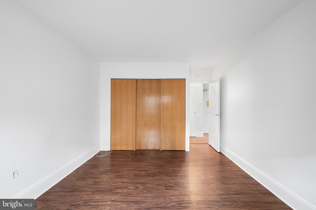 unfurnished bedroom featuring a closet, dark wood-style flooring, and baseboards