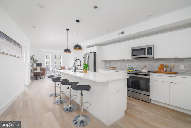 kitchen featuring light hardwood / wood-style flooring, decorative backsplash, an island with sink, white cabinetry, and stainless steel appliances