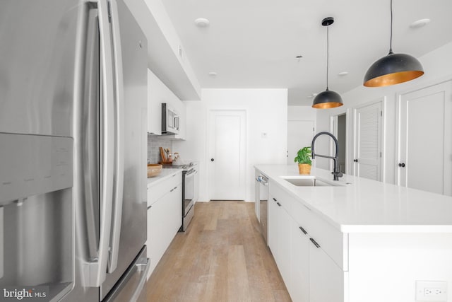 kitchen with light wood-type flooring, pendant lighting, white cabinets, sink, and stainless steel appliances