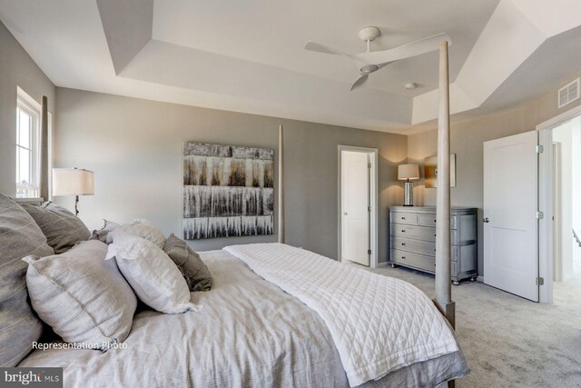 bedroom featuring a tray ceiling, light colored carpet, and ceiling fan