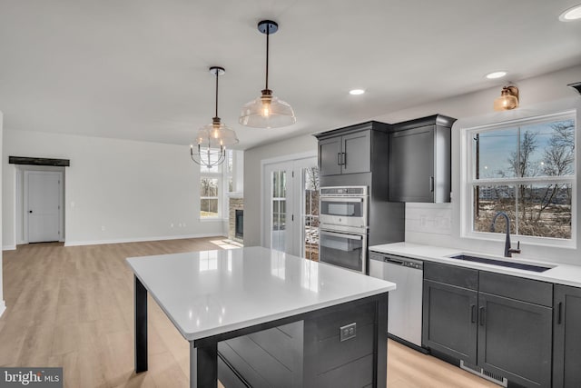 kitchen featuring a kitchen island, a sink, light countertops, appliances with stainless steel finishes, and decorative light fixtures