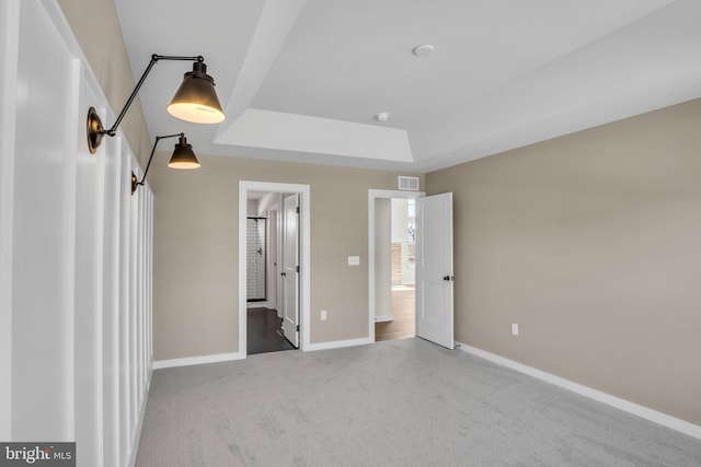 unfurnished bedroom featuring baseboards, visible vents, a raised ceiling, ensuite bath, and carpet floors