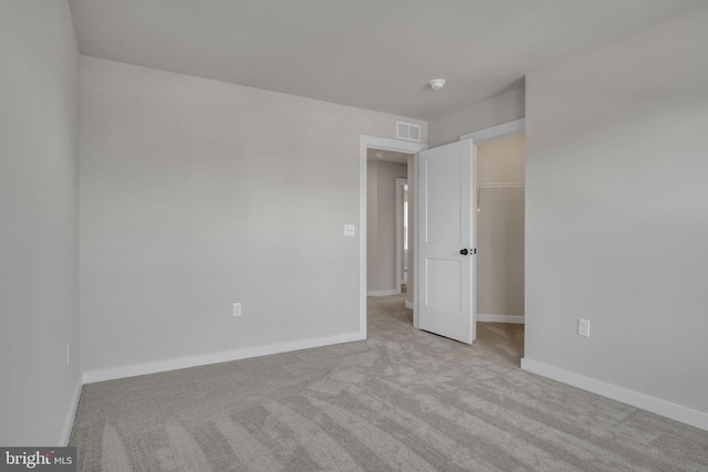 unfurnished bedroom with light carpet, baseboards, visible vents, a spacious closet, and a closet