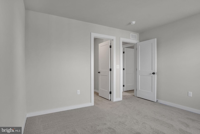 unfurnished bedroom with light carpet, baseboards, a spacious closet, and visible vents