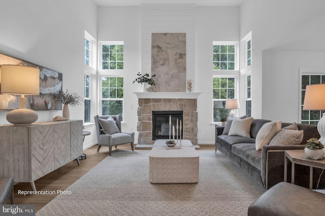 living area featuring light wood finished floors, a stone fireplace, a high ceiling, and baseboards