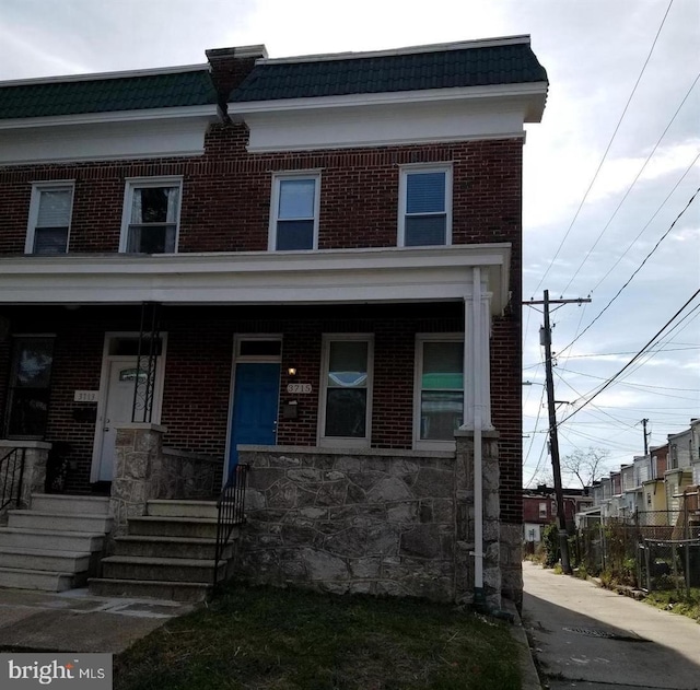 multi unit property with a porch, brick siding, and mansard roof