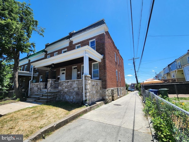 view of front of home featuring covered porch, fence, and brick siding