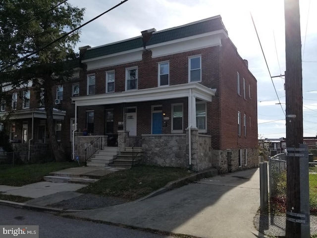 multi unit property with covered porch, brick siding, and mansard roof