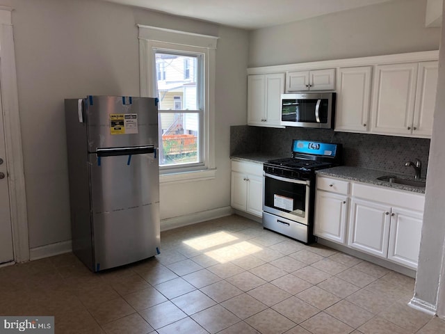 kitchen featuring light stone countertops, stainless steel appliances, a sink, white cabinets, and decorative backsplash