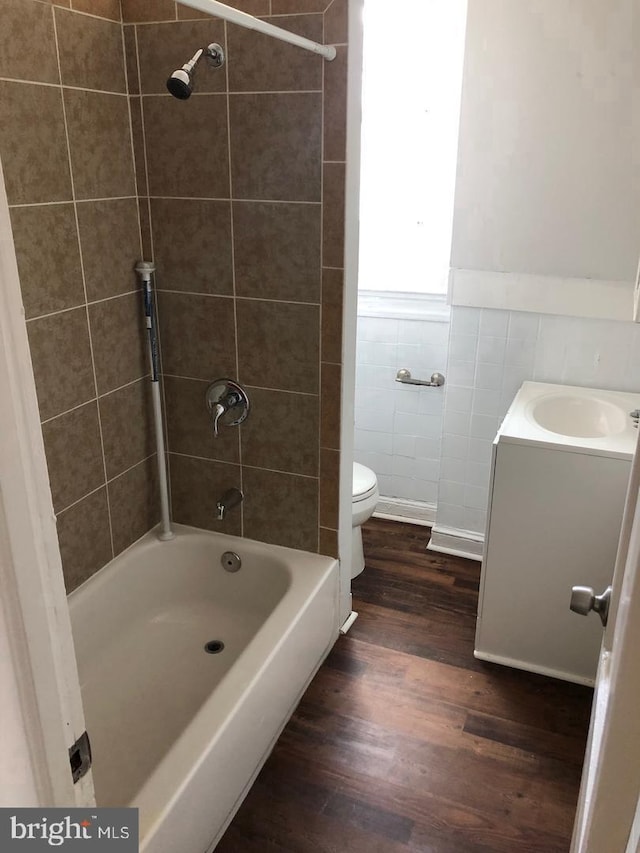 bathroom with toilet, a wainscoted wall, wood finished floors, vanity, and shower / washtub combination