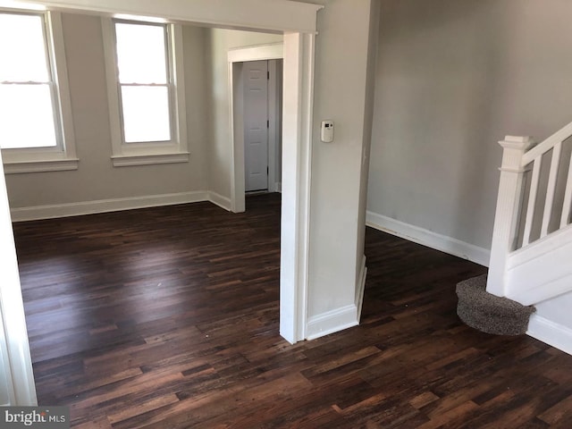 spare room featuring stairs, dark wood-type flooring, and baseboards