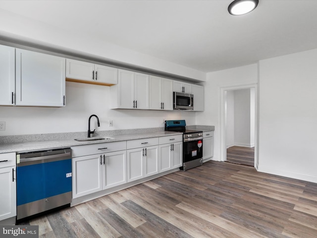 kitchen with a sink, white cabinetry, light countertops, appliances with stainless steel finishes, and light wood finished floors