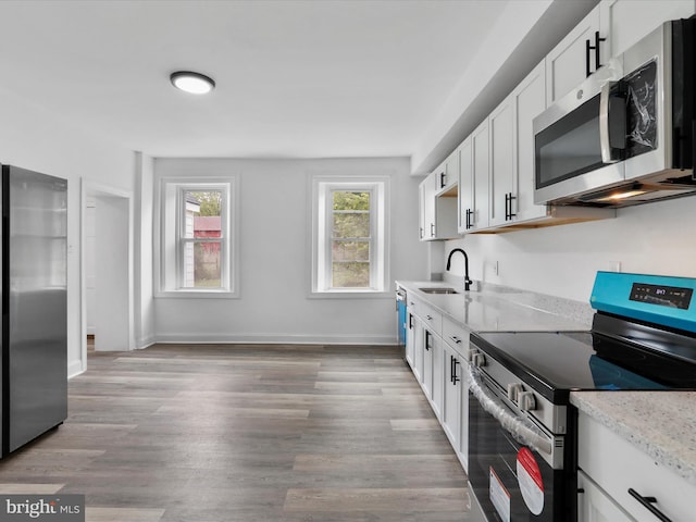 kitchen featuring light stone counters, a sink, white cabinetry, appliances with stainless steel finishes, and light wood-type flooring