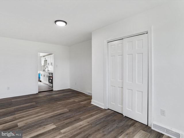 unfurnished bedroom with a closet, baseboards, visible vents, dark wood-type flooring, and a sink