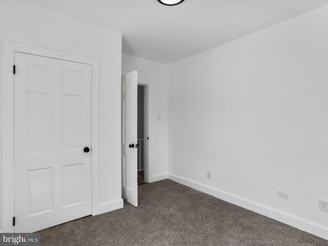 unfurnished bedroom featuring baseboards and dark colored carpet