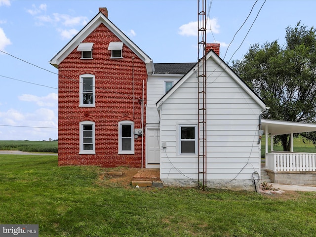 rear view of house with brick siding, a chimney, an attached carport, and a yard