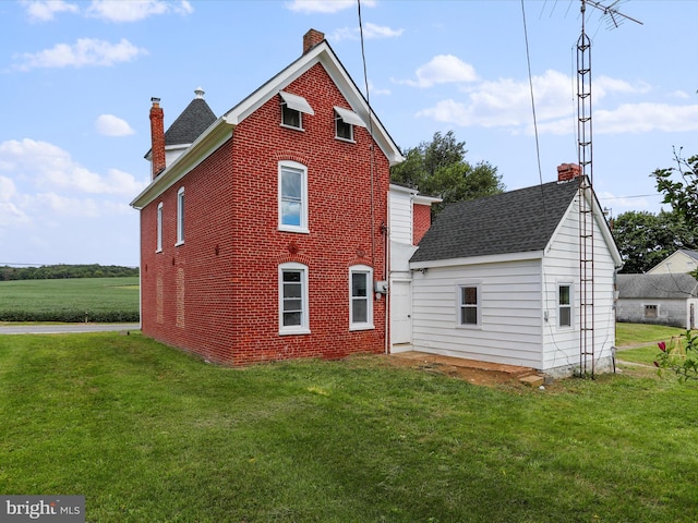 rear view of property with brick siding, a yard, and a chimney