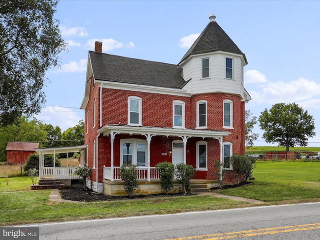 victorian house featuring a porch, brick siding, a shingled roof, a chimney, and a front yard