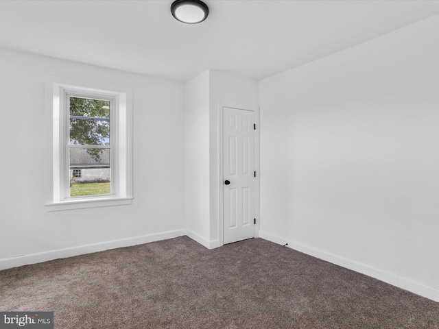 unfurnished room with dark colored carpet and baseboards