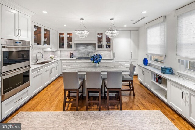 kitchen with a kitchen breakfast bar, light hardwood / wood-style flooring, a notable chandelier, a center island, and sink