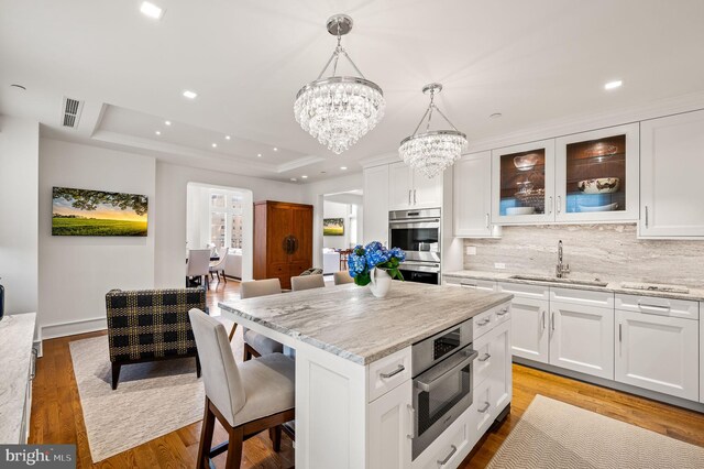 kitchen with a raised ceiling, light stone countertops, and white cabinetry