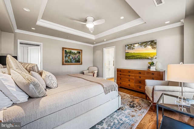 bedroom with ornamental molding, hardwood / wood-style flooring, a tray ceiling, and ceiling fan