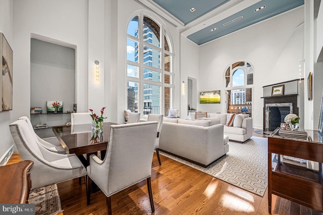 dining area with a fireplace, wood finished floors, and a towering ceiling