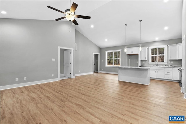 kitchen with hanging light fixtures, white cabinets, light wood-type flooring, a center island, and high vaulted ceiling