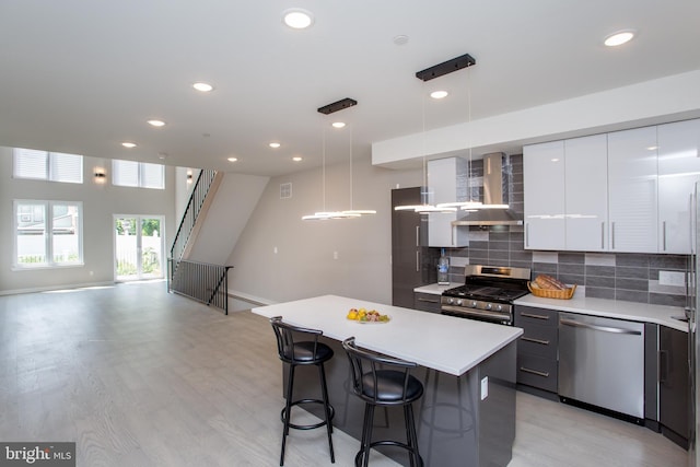 kitchen featuring wall chimney exhaust hood, pendant lighting, appliances with stainless steel finishes, a kitchen bar, and a center island