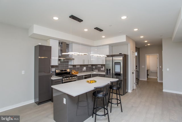 kitchen with wall chimney exhaust hood, light hardwood / wood-style flooring, appliances with stainless steel finishes, a center island, and hanging light fixtures