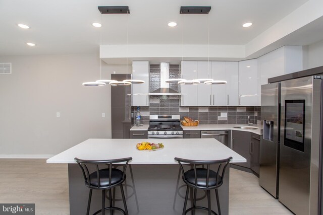 kitchen with wall chimney exhaust hood, decorative light fixtures, stainless steel appliances, and a kitchen island