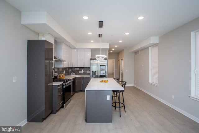 kitchen with a kitchen island, appliances with stainless steel finishes, hanging light fixtures, white cabinetry, and light wood-type flooring