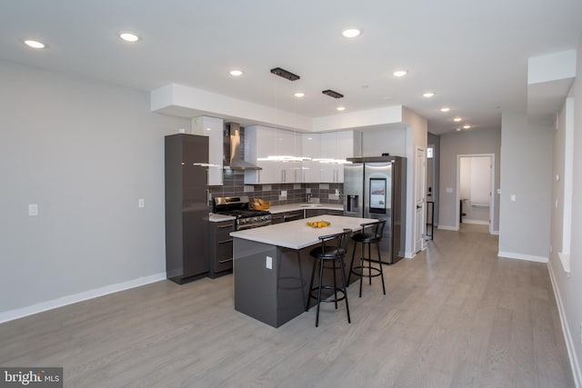 kitchen with a kitchen island, a breakfast bar area, light hardwood / wood-style floors, stainless steel appliances, and wall chimney range hood