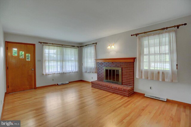 unfurnished living room featuring a wealth of natural light, a brick fireplace, and hardwood / wood-style floors