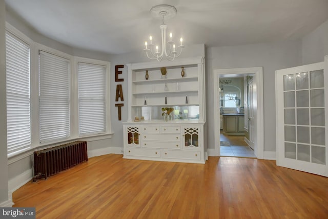 unfurnished dining area featuring a chandelier, light wood-type flooring, baseboards, and radiator