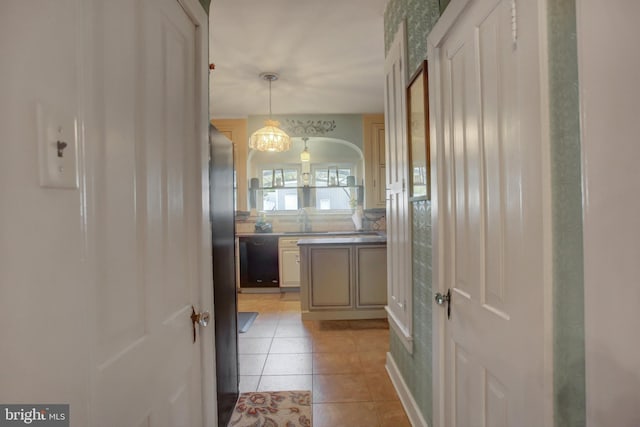 kitchen with light tile patterned floors, arched walkways, dishwasher, hanging light fixtures, and a sink