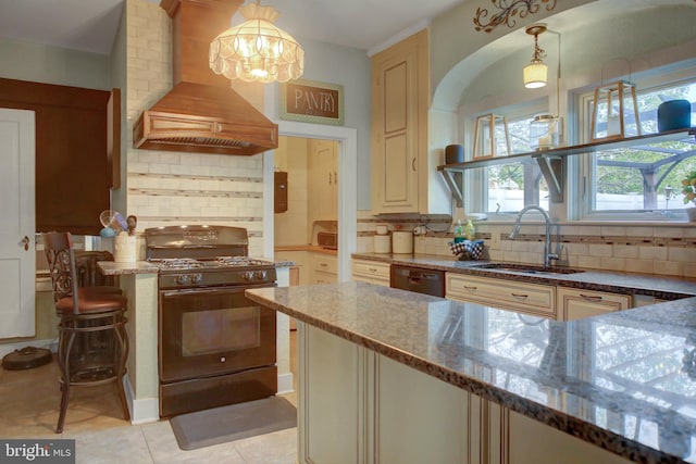 kitchen featuring dark stone counters, decorative light fixtures, black appliances, premium range hood, and a sink