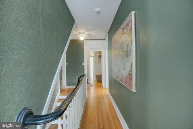 hallway featuring light wood-type flooring, baseboards, and an upstairs landing