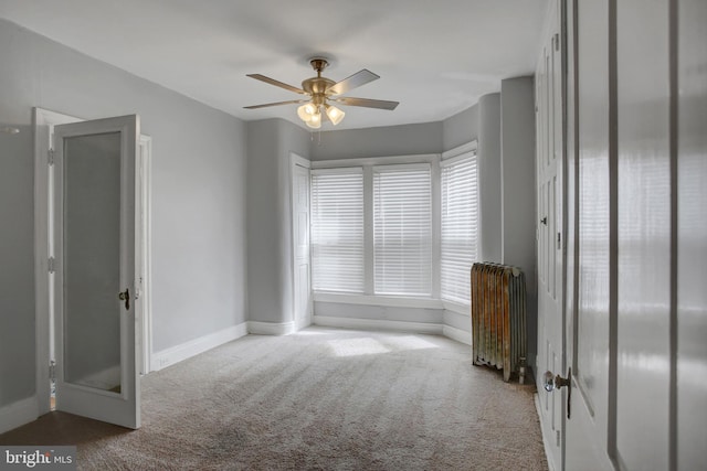 unfurnished bedroom featuring baseboards, ceiling fan, carpet, and radiator