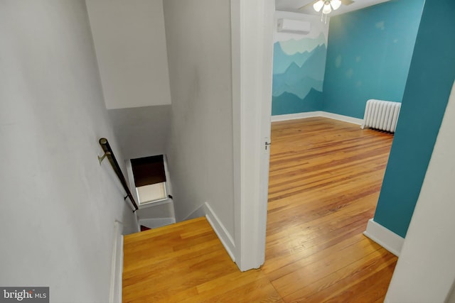 stairs with baseboards, radiator, ceiling fan, wood finished floors, and a wall mounted AC