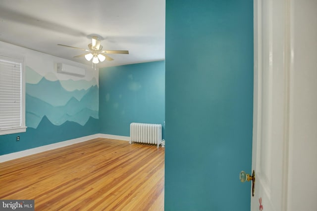 unfurnished room featuring a wall unit AC, wood finished floors, a ceiling fan, baseboards, and radiator heating unit