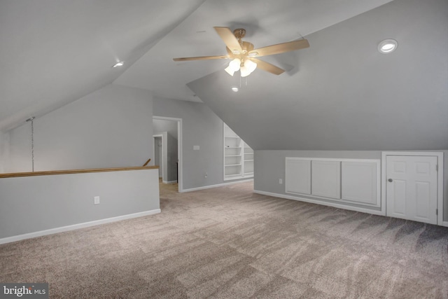 additional living space featuring baseboards, a ceiling fan, light colored carpet, lofted ceiling, and built in shelves