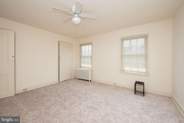 unfurnished bedroom with radiator heating unit, ceiling fan, and light colored carpet