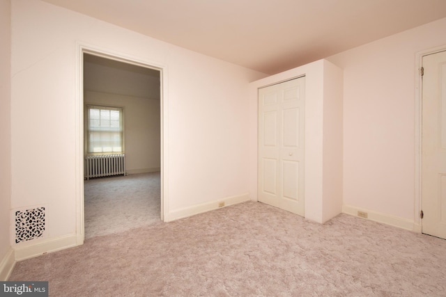 unfurnished bedroom with a closet, radiator, and light carpet