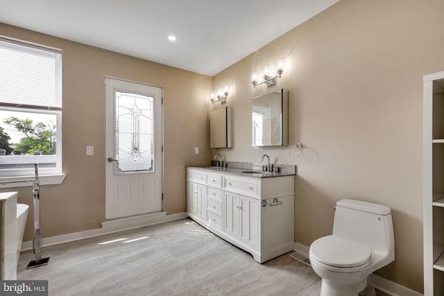 bathroom featuring toilet, a tub to relax in, and dual bowl vanity